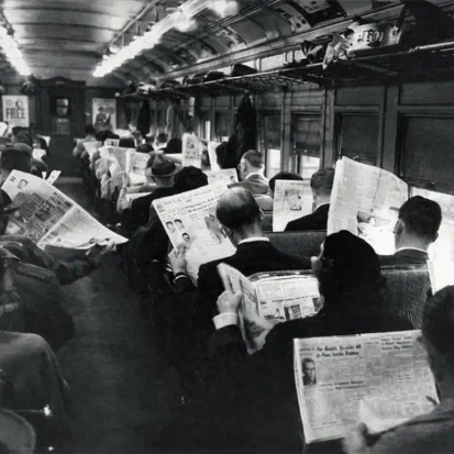 Een volle trein in de jaren '50, iedereen zit een krant te lezen en praat niet met elkaar.