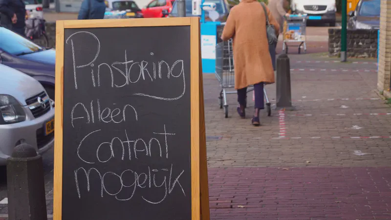 A Dutch shop with a sign about a nationwide PIN payment outage, causing customers to queue